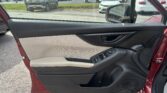 Driver's-side door interior in a red car, with window controls and beige armrest; dealership parking lot visible through the window.