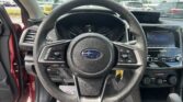 Driver’s view of the car interior: steering wheel, instrument cluster, and infotainment screen, with a parking lot seen through the windshield.