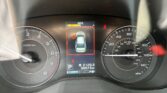 Car dashboard view: tachometer on left, speedometer on right, central digital display showing MPG and a blue car icon with red border.