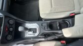 View of a car interior focusing on the center console: gear shifter, cup holders, and climate controls beside beige seats.