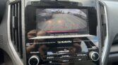 Rearview camera display showing parking lot with guiding green, yellow, and red lines for backing up; Subaru dashboard visible.