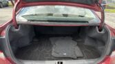 Open trunk of a red car showing black carpeted interior and several floor mats inside the cargo area.