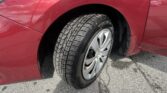 Close-up of a red car's front left wheel and tire, showing tread pattern and fender edge I