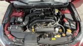 Open hood showing engine bay of a red car with air intake, hoses, and reservoirs visible behind windshield wipers