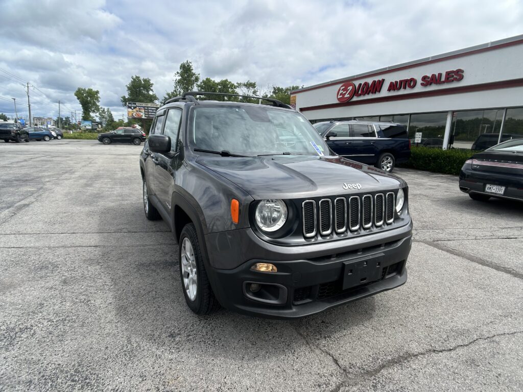 Front view of a gray Jeep Wrangler parked in a car lot next to EZ Loan Auto Sales storefront on a cloudy day