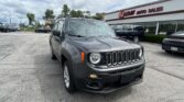 Front view of a gray Jeep Wrangler parked in a car lot next to EZ Loan Auto Sales storefront on a cloudy day