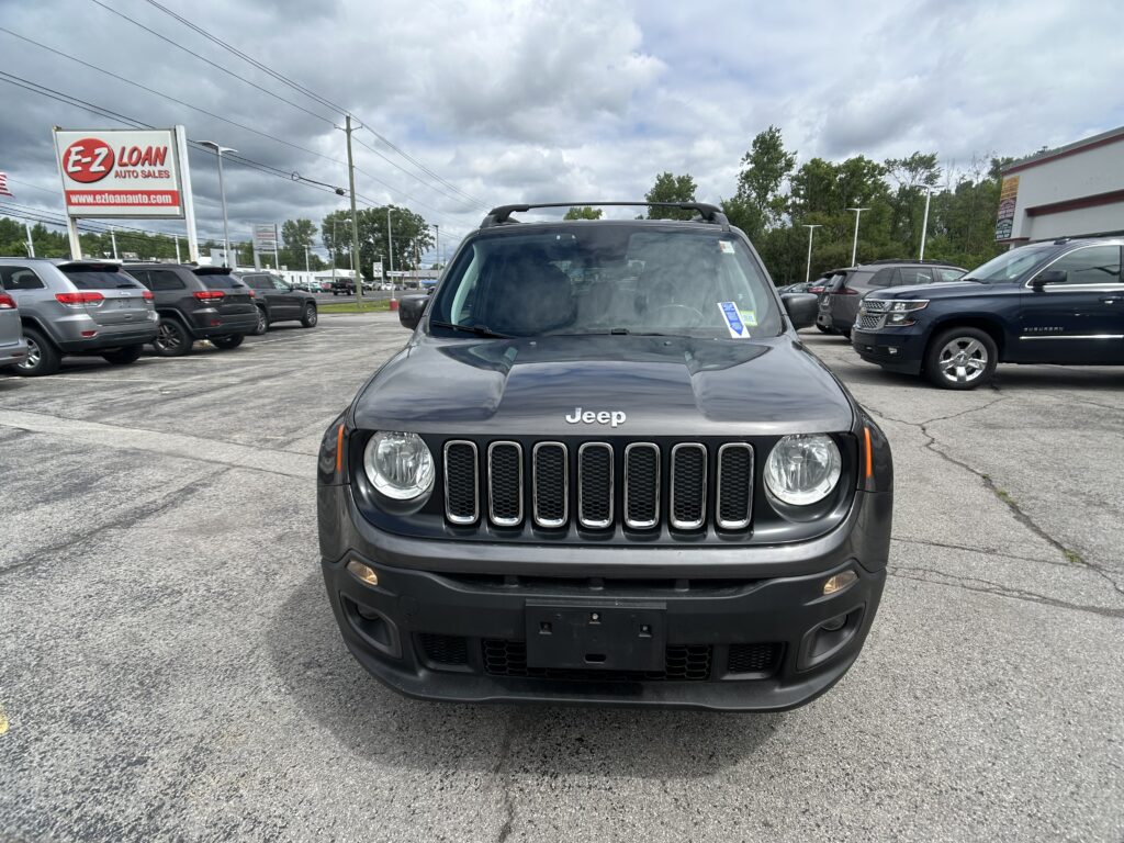 Front view of a dark gray Jeep SUV in a dealership parking lot with an EZ LOAN sign in the background.