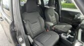 Interior of a black fabric car: front seats with center console, steering wheel visible, driver’s door open, parking lot outside.