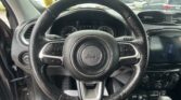 View from the driver’s seat showing a Jeep steering wheel, instrument cluster, and center console with a parking lot visible through the windshield.