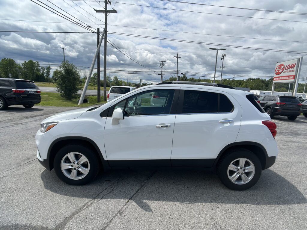 White SUV in a dealership lot with power lines above and an EZ LOAN Auto Sales sign in the distance, cloudy sky.