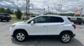 White SUV in a dealership lot with power lines above and an EZ LOAN Auto Sales sign in the distance, cloudy sky.