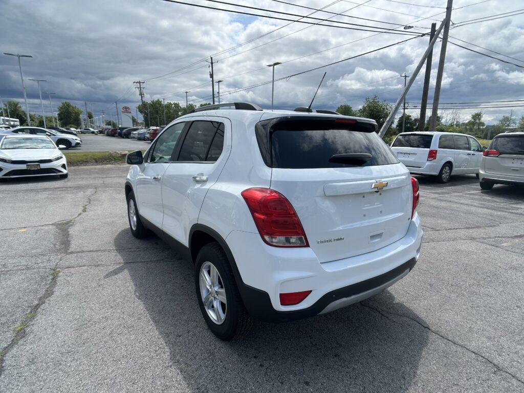 White Chevrolet Trax SUV in a car dealership lot with other vehicles and a cloudy sky overhead