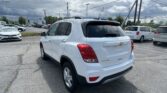 White Chevrolet Trax SUV in a car dealership lot with other vehicles and a cloudy sky overhead