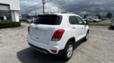 Rear three-quarter view of a white SUV in a dealership lot with other cars under a cloudy sky, left building in frame.