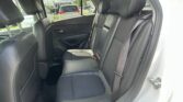 Back seat of a car with black leather upholstery, three headrests, and visible seat belts; outside view shows parked vehicles through the window.