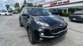 Black Kia SUV in the foreground at EZ Loan Auto Sales lot with other cars and the dealership building in the background, blue sky overhead.