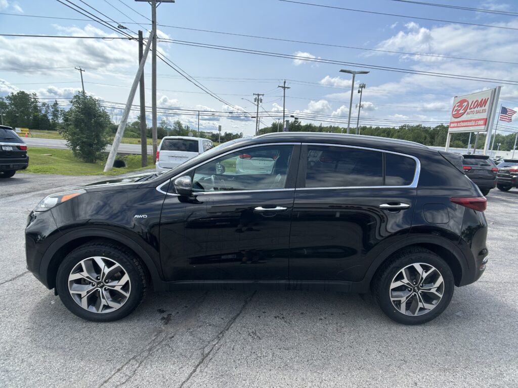 Black Kia SUV in a dealership lot, foreground, with power lines and an EZ Loan Auto Sales sign in the background on a sunny day.