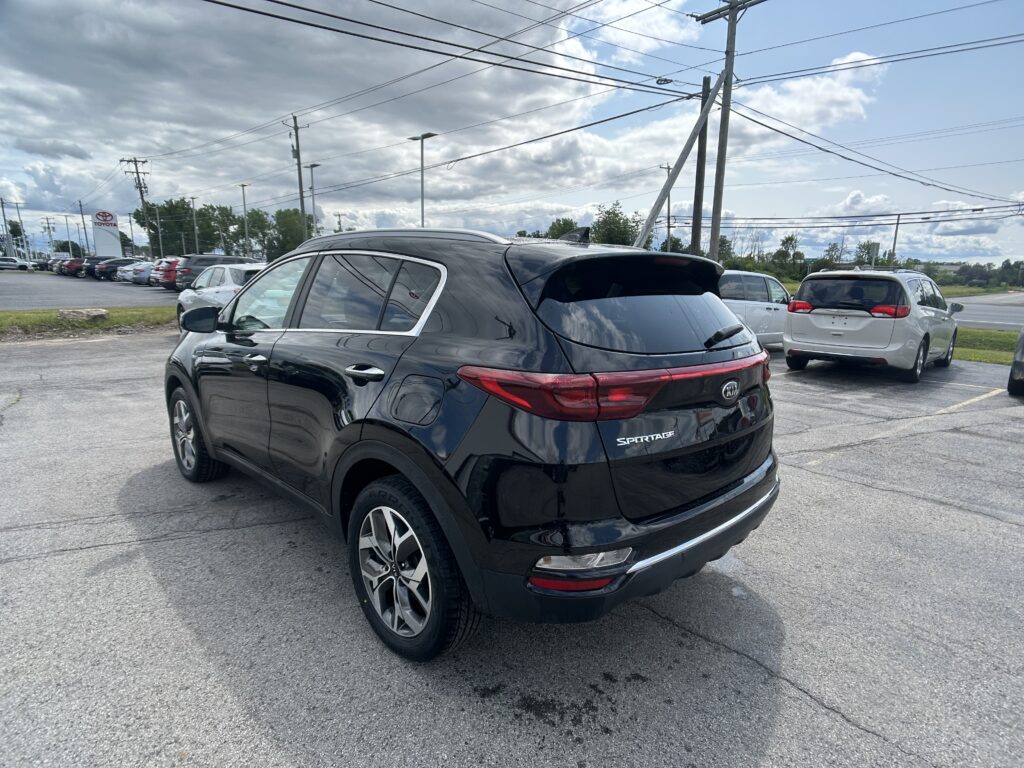 Black Kia Sportage in a parking lot with other cars, power lines overhead and a Toyota dealership sign in the distance.