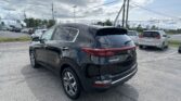 Black Kia Sportage in a parking lot with other cars, power lines overhead and a Toyota dealership sign in the distance.