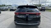 Rear view of a black Kia Sportage EX parked in a car lot with other vehicles and a cloudy sky above.