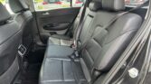 Rear seating area of a car with black leather seats, visible seat belts, and headrests; parking lot seen through windows.