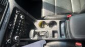 Car center console with gear shift, climate controls, cup holders, and black leather seats, shot from above between front seats.