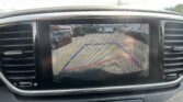 Rearview camera display showing parking guides and a street scene behind the car, reminding to check surroundings for safety.