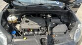 Open car hood showing the engine bay with the coolant reservoir, battery, and various hoses visible under the hood of a Kia.