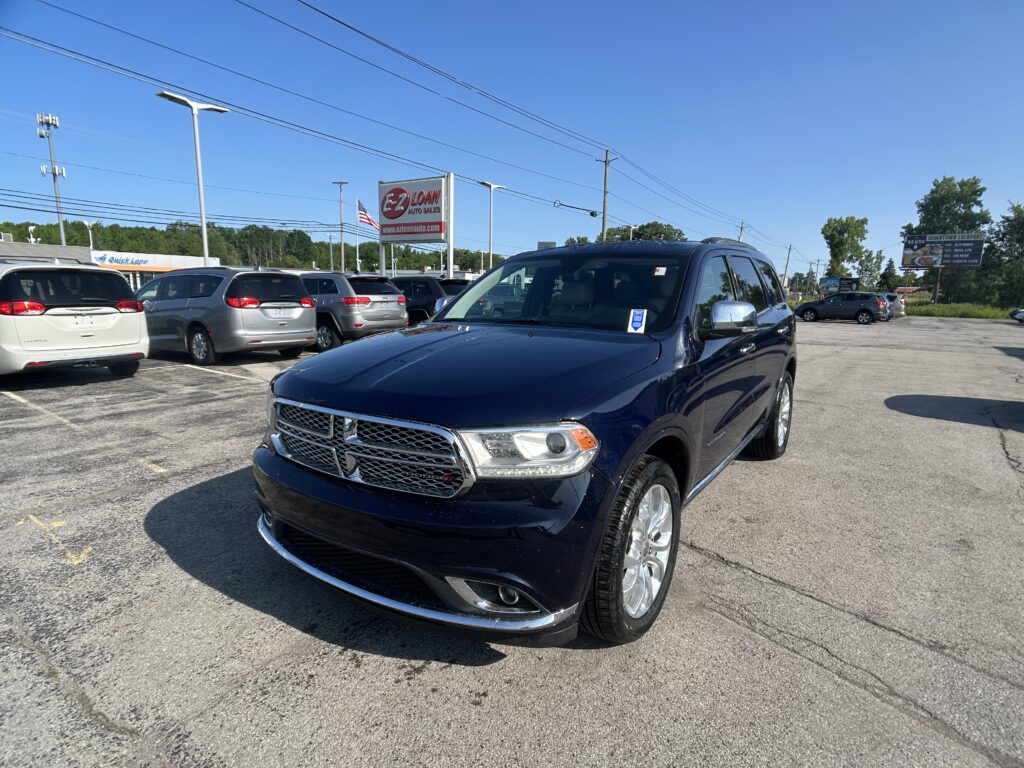 Blue Dodge SUV in a dealership parking lot with other minivans and an EZ Auto Sales sign in the background on a sunny day