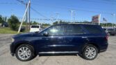 A dark blue SUV parked in a dealership lot with tall power lines and utility poles overhead, and a roadside sign in the background.