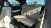 Rear row of tan leather car seats in an SUV, with sunlight through the windows outside.]**