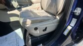Beige leather driver and front passenger seats with center console and open car door on a blue vehicle exterior viewed from the passenger side key area.