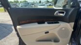 Interior of an open car door showing beige and black panel with chrome handle and window controls; parking lot full of cars outside.