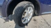Close-up of a blue SUV's wheel and tire in the wheel well, with wet mud splashes on the fender and body panel edge.