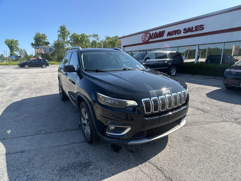 Dark gray Jeep SUV in the dealership lot with EZ Loan Auto Sales storefront in the background on a sunny day.