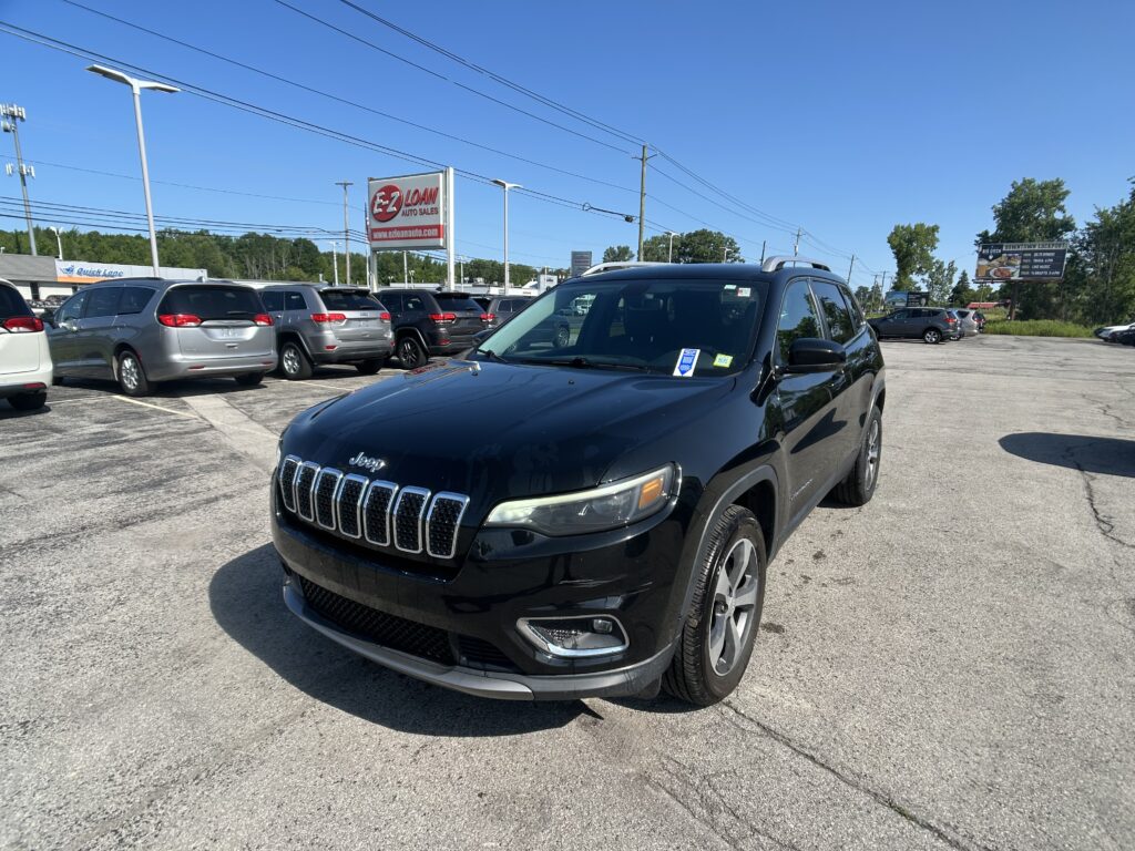 Black Jeep SUV in a dealership lot with rows of minivans and an EZ Loan Auto Sales sign in the background.