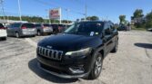 Black Jeep SUV in a dealership lot with rows of minivans and an EZ Loan Auto Sales sign in the background.