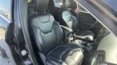 Open passenger door view of a Jeep interior with black leather front seats and center console visible in daytime light.