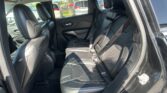 Rear seat area of a black leather SUV with three seats, headrests, and visible seat belts; outside parking lot visible through the windows.