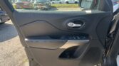 Interior of a car door with window controls and a side mirror, looking out onto a parking lot of parked cars.