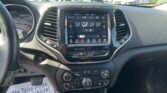 Vehicle interior with a center touchscreen climate control panel, steering wheel to the left, and a gear shifter, view of a dealership lot through the windshield.