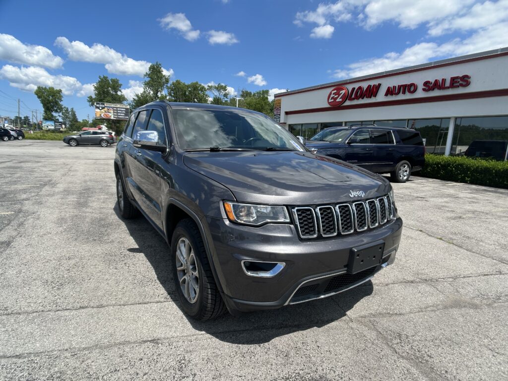 Gray Jeep SUV parked in a dealership lot with the EZ Loan Auto Sales building and sign in the background under a blue, partly cloudy sky