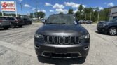 Front view of a dark gray Jeep SUV in a dealership lot, with a bright blue sky and 'E-Z Loan Auto Sales' sign in the background