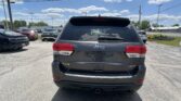 Rear view of a gray Jeep SUV in a dealership parking lot, with other cars and a clear blue sky above.