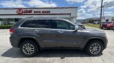 Gray SUV (Jeep Grand Cherokee) parked in front of a white auto dealership building with 'E-Z LOAN Auto Sales' sign on a sunny day
