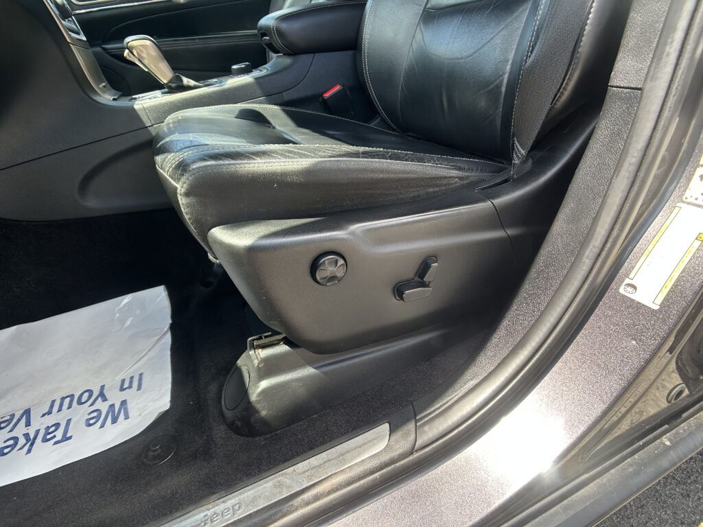 Black leather car interior focusing on the driver’s seat side with power-adjustment controls and the center console nearby.