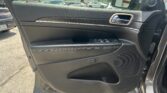Inside a car door showing the armrest with window controls, chrome door handle, and a speaker, with a parking lot visible outside the window.