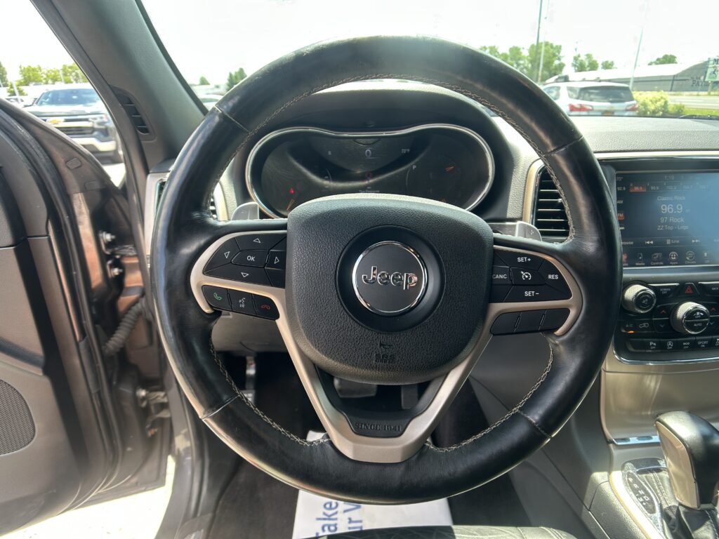 Close-up of a Jeep steering wheel with the instrument cluster and center console visible, parked in a lot outside the car.