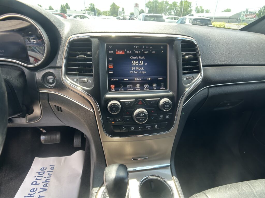Center console view: touchscreen radio showing Classic Rock at 96.9, flanked by air vents and climate controls, with cupholders and gear shifter nearby in daylight driving interior.