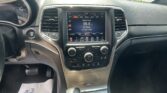 Center console view: touchscreen radio showing Classic Rock at 96.9, flanked by air vents and climate controls, with cupholders and gear shifter nearby in daylight driving interior.